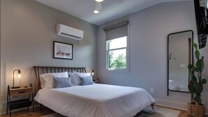 Ein Schlafzimmer mit einem großen Bett, einem Nachttisch, einer Wand-Klimaanlage, einem Fenster und einem Spiegel.