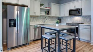 A modern kitchen with white cabinets, stainless steel appliances, a wooden table, and bar stools.
