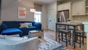 A modern living room with a blue sofa, a coffee table, and a dining area with a kitchen in the background.