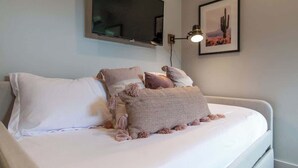 A bedroom with a bed, a mounted TV, a framed picture, and a wall-mounted lamp.