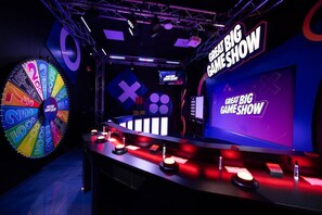 A game show set with a large wheel, a desk with game elements, and a sign reading "GREAT BIG GAME SHOW".