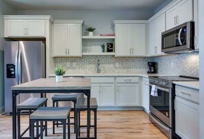 A modern kitchen with white cabinets, a stainless steel refrigerator, a microwave, and an oven.
