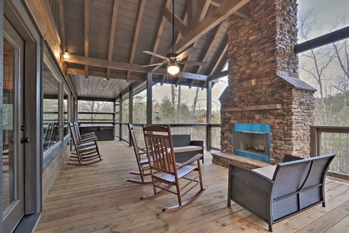 A covered outdoor area with a stone fireplace, wooden furniture, and a ceiling fan.