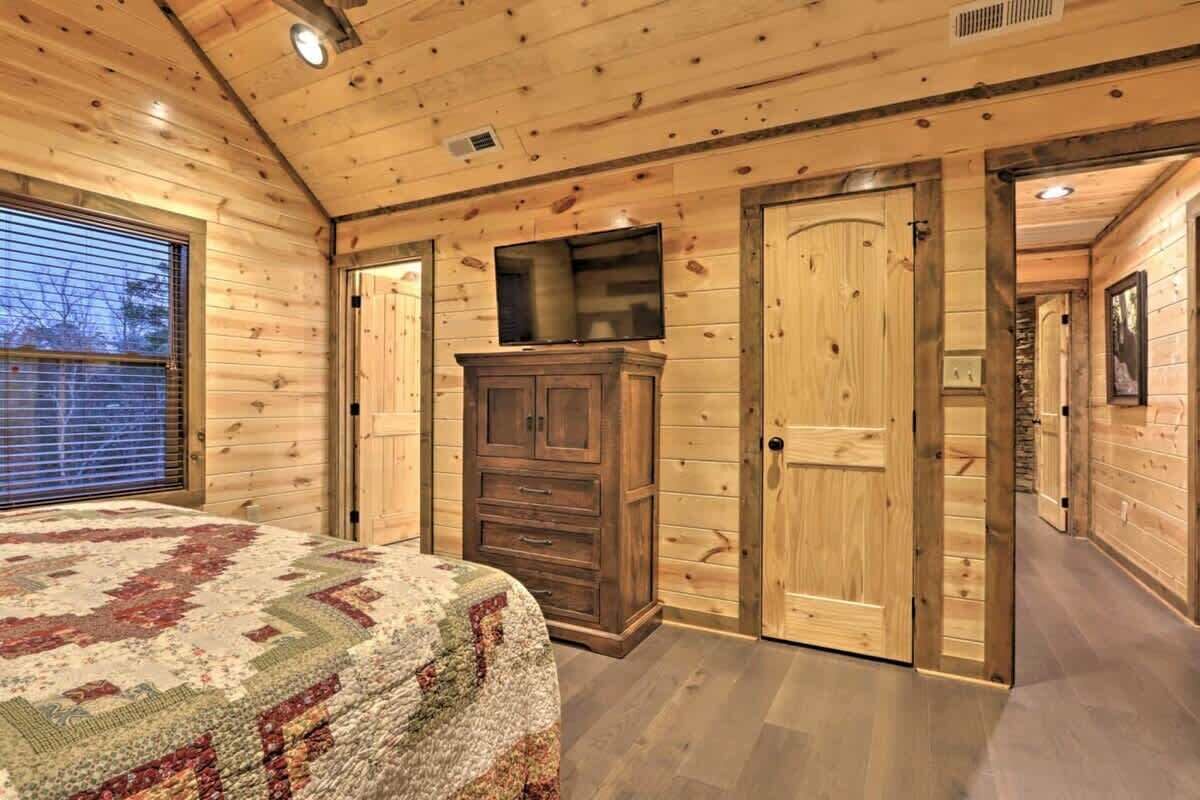 Ein gemütliches Schlafzimmer in einer Holzhütte mit einem Bett, einem an der Wand montierten Fernseher und einem großen Holzschrank.