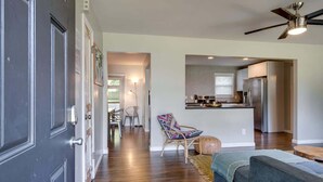 Una sala de estar moderna con un sofá, un comedor con sillas, una cocina con refrigerador y un ventilador de techo.