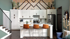 A modern kitchen with white cabinets, a central island with bar stools, and a wooden slatted wall above. - Stay In The Heart Of 12 South, Designer Penthouse  |  1 of 7 Themed Lofts at Cowrite, Find Coffee and Tacos Downstairs, Complimentary Spin Class, Walk to Shopping in 12 South, 10 Minutes to Broadway, Parking, 24 Hr Hospitality (Nashville)