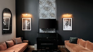 A modern living room with a black piano, two sofas, framed artwork, and a large TV on the wall. - Johnny Cash Inspired 2-Suite Loft In 12 South      |         1 of 7 Themed Lofts at Cowrite, Find Coffee and Tacos Downstairs, Complimentary Spin Class, Walk to Shopping in 12 South, 10 Minutes to Broadway, Parking, 24 Hr Hospitality (Nashville)