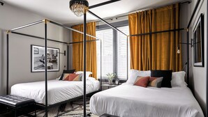 Een slaapkamer met twee bedden, een zwart metalen hemelbed, een zwarte lederen bank en een kroonluchter.