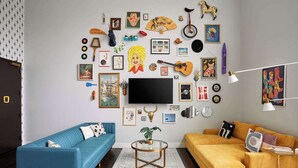 Un salon avec un canapé bleu, un canapé jaune, une table basse et un téléviseur fixé au mur.