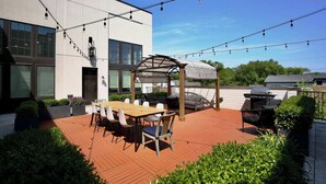 Une terrasse extérieure avec une table et des chaises en bois, une pergola et un barbecue.