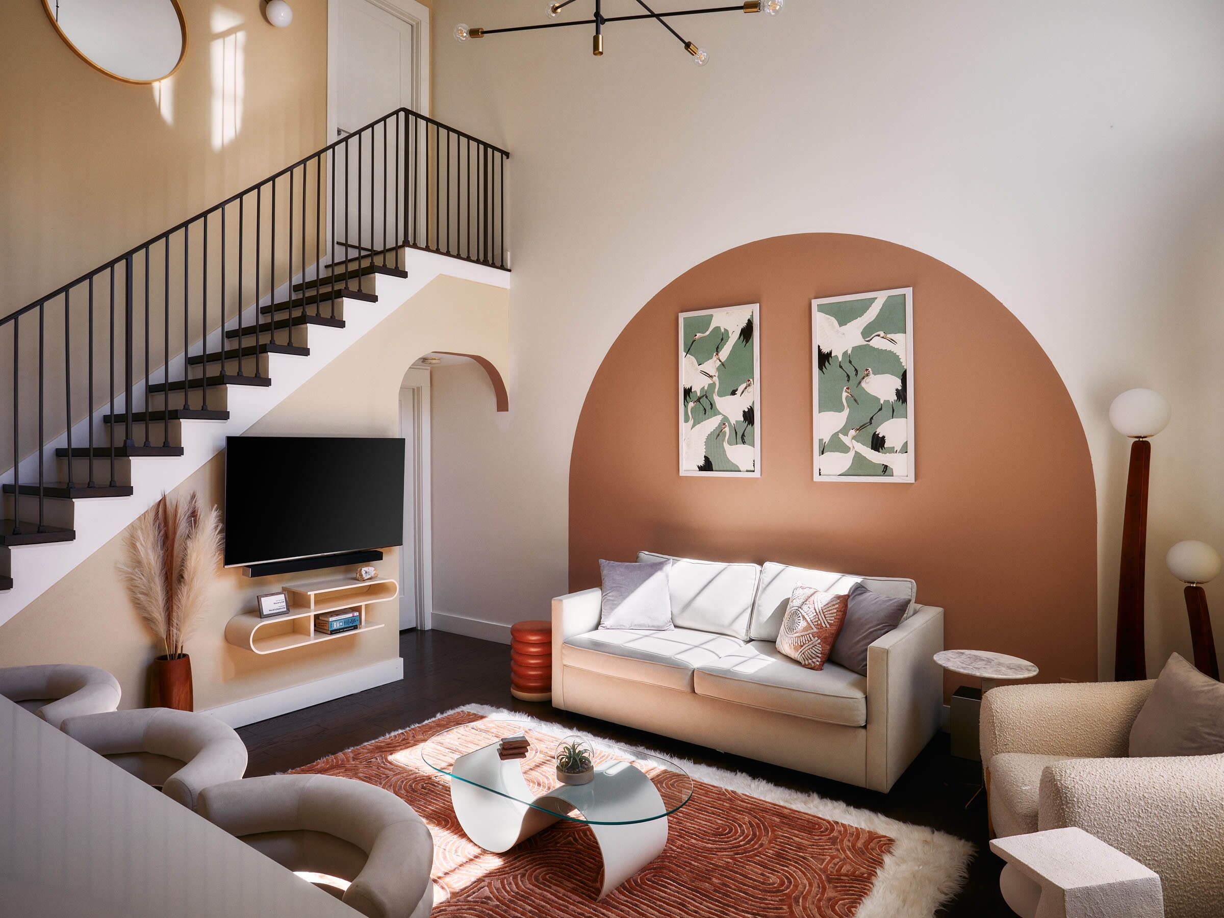 Un salon moderne avec un escalier, un téléviseur à écran plat, un canapé et deux œuvres d’art accrochées au mur.