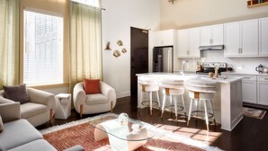 A modern living room with a glass coffee table, two white bar stools, a beige sofa, and a small side table. - King Penthouse in 12 South, 3 Miles To Broadway   |   Soaring Ceilings, 1 of 7 Themed Lofts at Cowrite, Find Coffee and Tacos Downstairs, Complimentary Spin Class, Walk to Shopping in 12 South, 10 Minutes to Broadway, Parking, 24 Hr Hospitality (Nashville)
