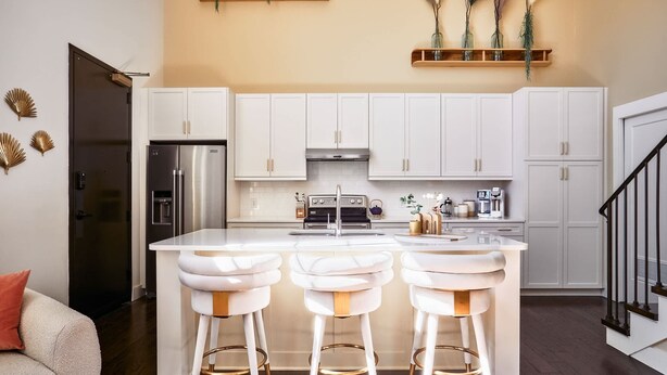 A modern kitchen with white cabinets, a stainless steel refrigerator, a central island with bar stools, and decorative plants on shelves. - King Penthouse in 12 South, 3 Miles To Broadway   |   Soaring Ceilings, 1 of 7 Themed Lofts at Cowrite, Find Coffee and Tacos Downstairs, Complimentary Spin Class, Walk to Shopping in 12 South, 10 Minutes to Broadway, Parking, 24 Hr Hospitality (Nashville)