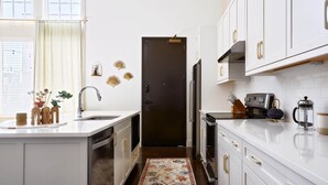 A modern kitchen with white cabinetry, a central island, and a dark door. - King Penthouse in 12 South, 3 Miles To Broadway   |   Soaring Ceilings, 1 of 7 Themed Lofts at Cowrite, Find Coffee and Tacos Downstairs, Complimentary Spin Class, Walk to Shopping in 12 South, 10 Minutes to Broadway, Parking, 24 Hr Hospitality (Nashville)
