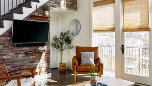 Un salon spacieux avec un mur en briques, un escalier, un téléviseur à écran plat, un fauteuil en cuir confortable et une grande fenêtre offrant une belle vue.