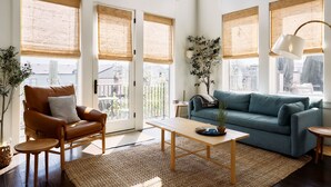 Un salon spacieux avec de grandes fenêtres, un fauteuil en cuir, un canapé de couleur turquoise et une table basse en bois.