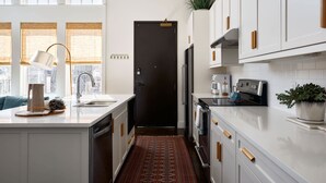 Une cuisine moderne avec des meubles blancs, une porte noire, une machine à café et une plante en pot.