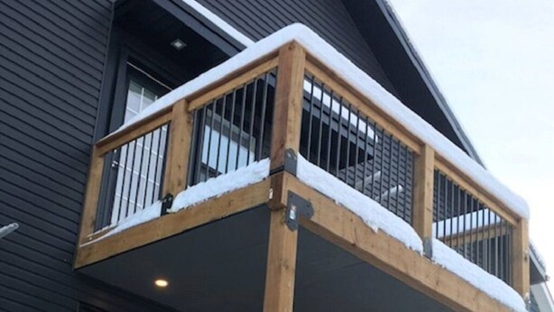 Eine mehrstufige Holzterrasse mit Geländern, bedeckt mit Schnee, an ein dunkel gefärbtes Gebäude angebaut.