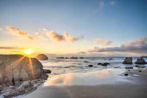 Une plage avec de gros rochers et des eaux calmes au coucher du soleil.