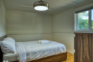 A single bed with white linens in a room with a wooden headboard and a window. - Suite 206: Beautiful 2-Bedroom Beachfront Suite (Wainfleet)