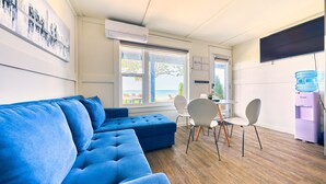 A modern living room with a blue sectional sofa, a dining table with chairs, and a water dispenser. - Suite 206: Beautiful 2-Bedroom Beachfront Suite (Wainfleet)