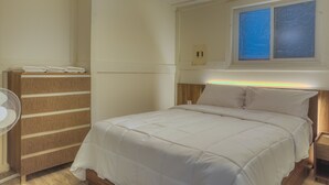 A bedroom with a bed, a wooden wardrobe, a bedside table, a nightstand, and a window with frosted glass. - Suite 206: Beautiful 2-Bedroom Beachfront Suite (Wainfleet)