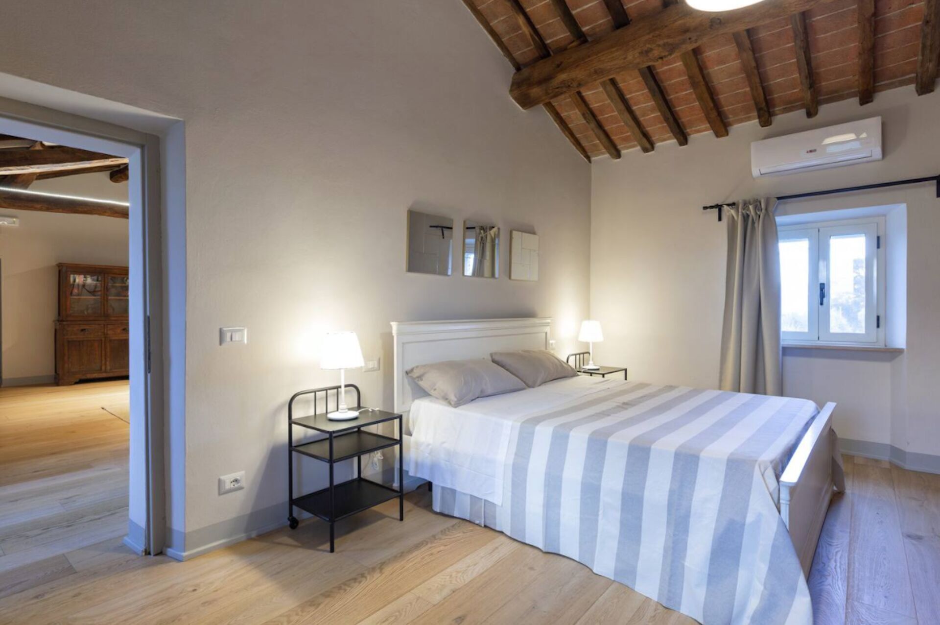 Une chambre à coucher avec un lit, deux tables de chevet avec des lampes, une fenêtre avec des rideaux et un plafond en bois.