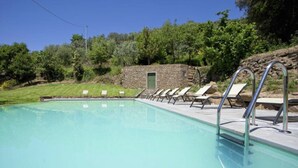 Piscina com espreguiçadeiras e um edifício de pedra ao fundo.