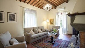 Uma sala de estar com sofá, poltronas, tapete estampado, mesa com abajur e lareira.