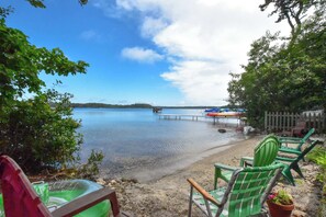 A beach with green chairs and a dock extending into calm water.