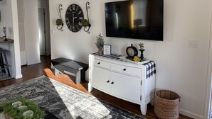 A modern living room with a flat-screen TV, a white cabinet, a patterned rug, and a decorative clock.