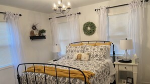 A neatly arranged bedroom with a bed, bedside table, lamp, and a small shelf.