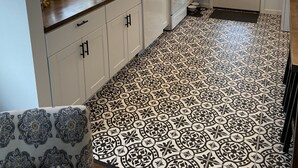 A kitchen with white cabinets, a black and white patterned floor, and a window with sheer curtains.