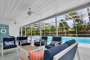 A covered outdoor seating area with a pool, white ceiling, and large windows.