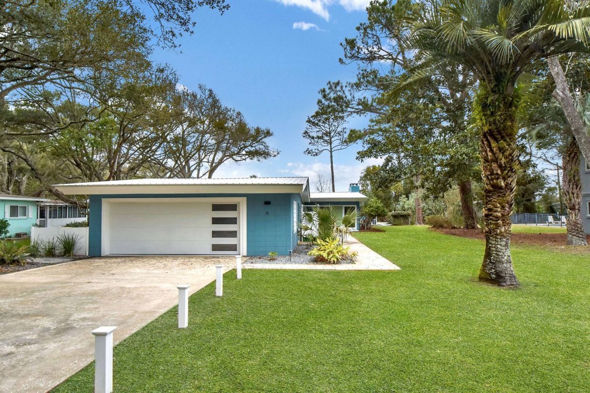 Une maison de plain-pied avec un garage, entourée d’une pelouse bien entretenue et de palmiers.