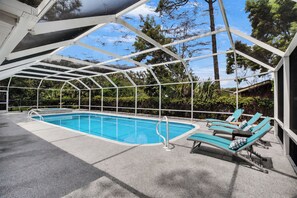 A covered outdoor swimming pool with lounge chairs and a glass ceiling structure.