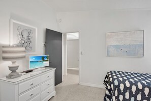 Un dormitorio con cama, televisión, cómoda y obras de arte en las paredes.