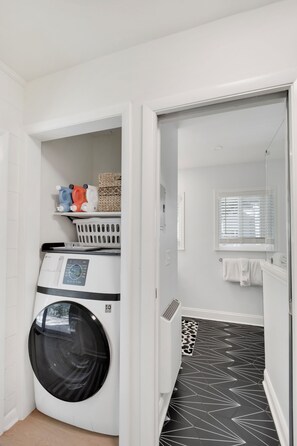 A laundry room with a front-loading washing machine, a basket, and a shelf with laundry items.