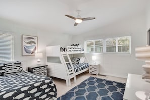 A bedroom with bunk beds, a ceiling fan, a window with blinds, and a framed picture on the wall.
