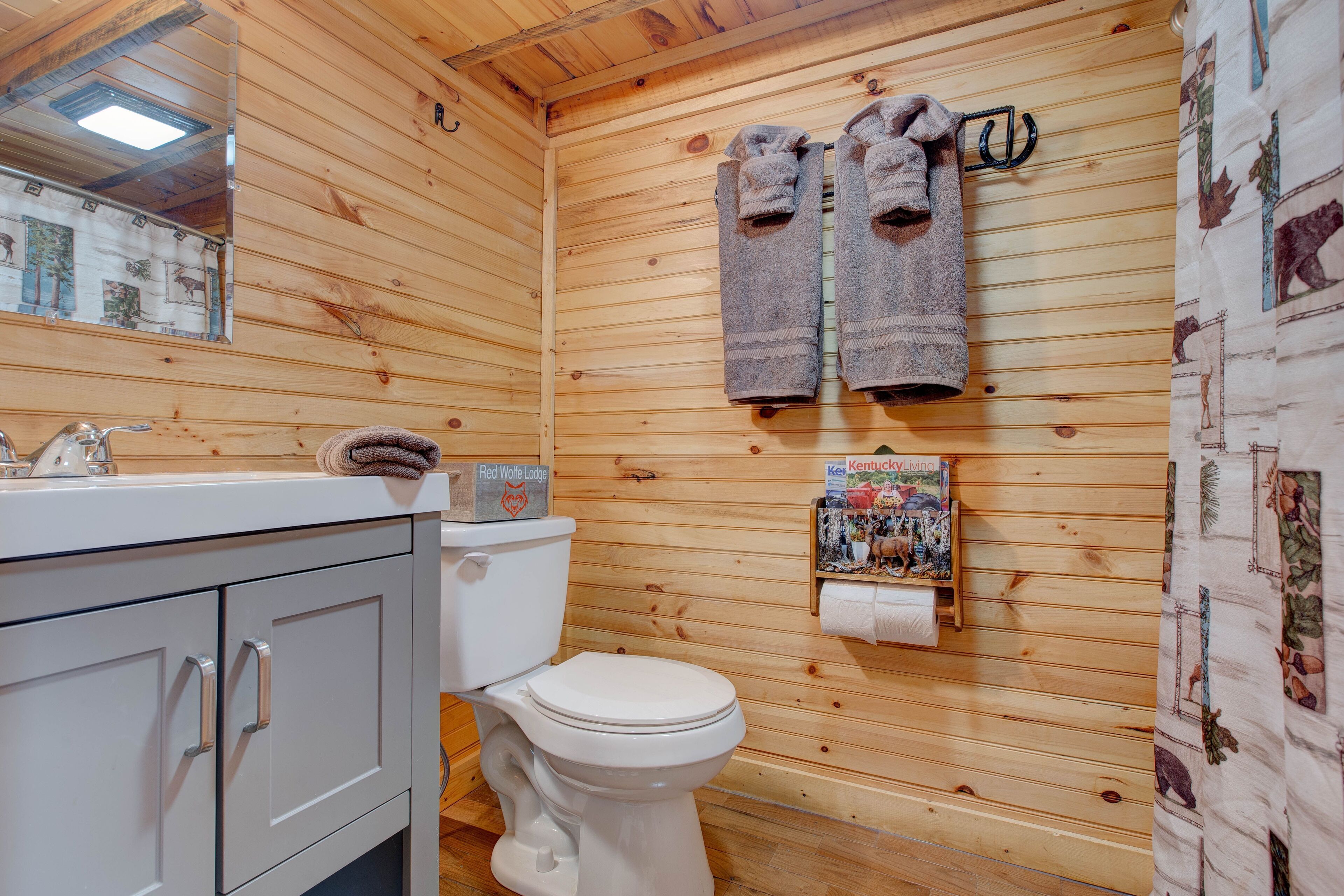 A wooden cabin bathroom with a toilet, sink, and cabinets.