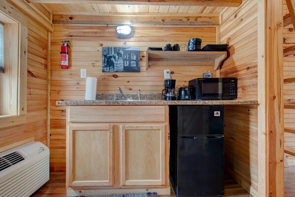 A compact kitchen with wooden walls, a built-in microwave, a black refrigerator, a coffee maker, and a fire extinguisher. - Hikers Retreat• Handcrafted Cabin in RRG • PET FRIENDLY• Location is Key (Pine Ridge)