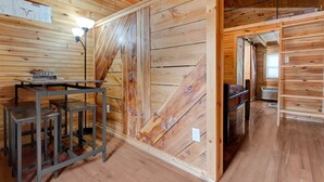 A wooden interior with a table and stools, a wall with a diagonal wooden panel, and a ceiling with exposed beams. - Hikers Retreat• Handcrafted Cabin in RRG • PET FRIENDLY• Location is Key  (Pine Ridge)