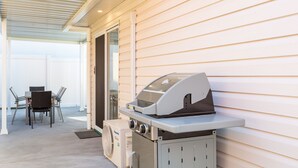 Un patio exterior con una parrilla, una mesa y sillas, y un ventilador.
