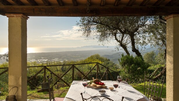Un área de comedor al aire libre con una mesa dispuesta para dos, con vistas a un paisaje pintoresco con colinas y una masa de agua.