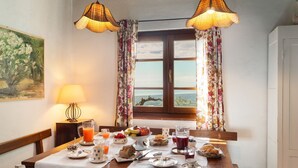 Un comedor con una mesa dispuesta para el desayuno, que incluye frutas, pasteles y bebidas diversas.