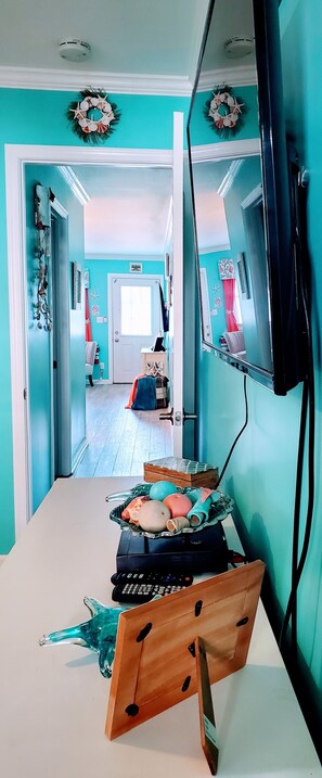 A room with teal walls, a wooden dining table, a TV mounted on the wall, and a door leading to another room.