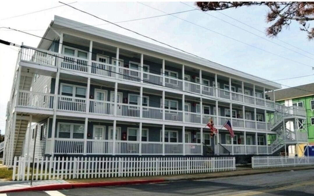 A multi-story hotel with balconies, a white picket fence, and two flags.