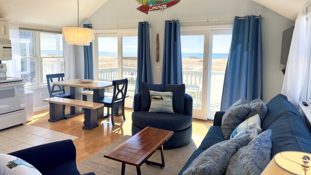 A cozy living room with a view of the beach, a dining area, and a kitchenette. - Beachfront on our private beach!  Siren Cottage - Pipers' Shore (North Truro)