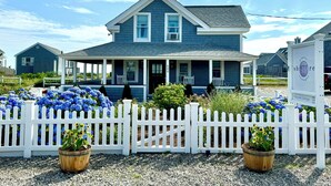 A two-story house with a porch, surrounded by a white picket fence and potted plants. - Beachfront on our private beach!  Siren Cottage - Pipers' Shore (North Truro)