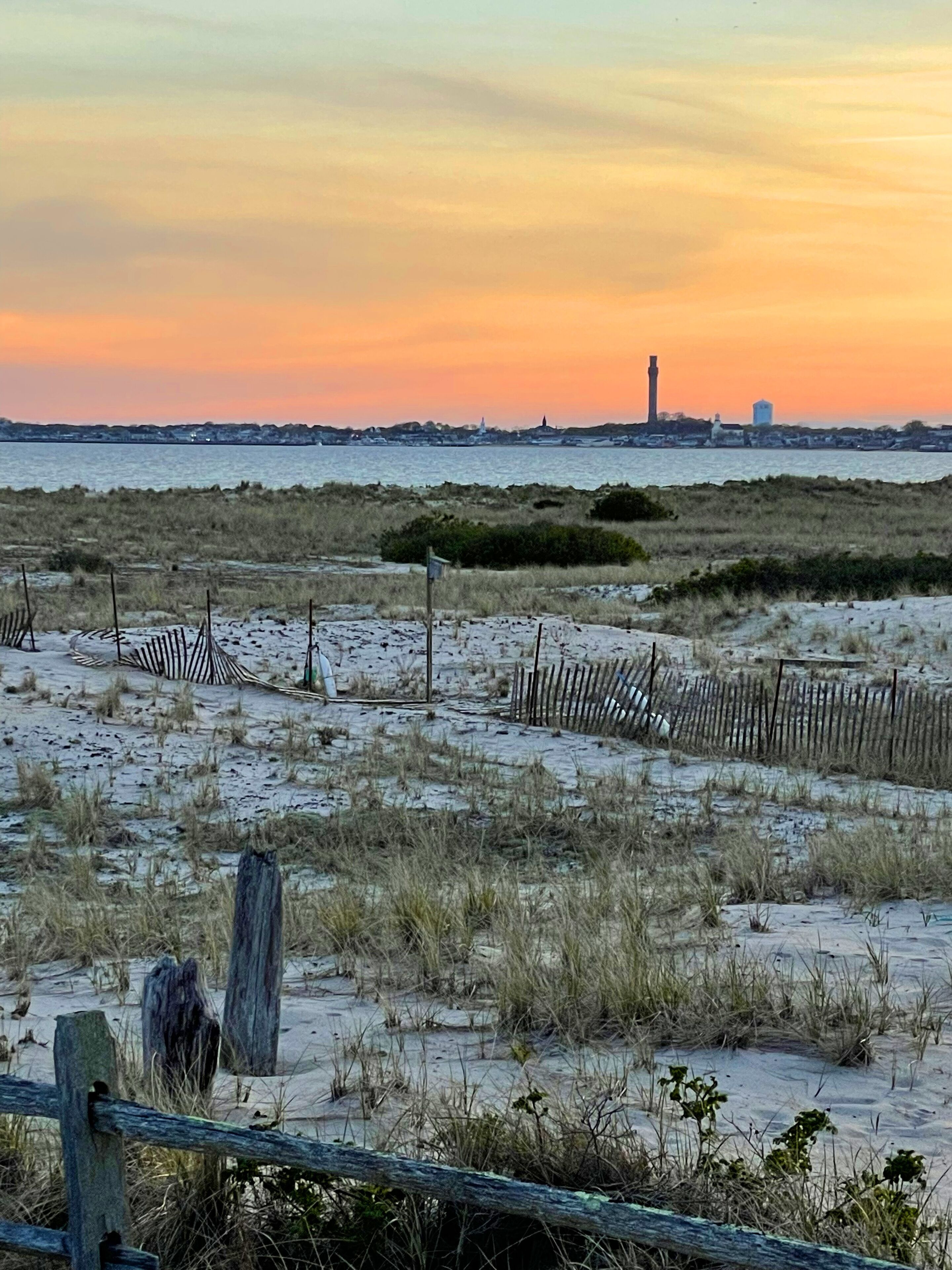 A beach with a wooden fence, sandy dunes, and a distant lighthouse.